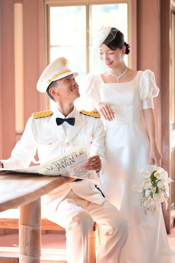異人館の窓辺で微笑み合う新郎新婦|白い制服とドレスが光に包まれる洋館フォト