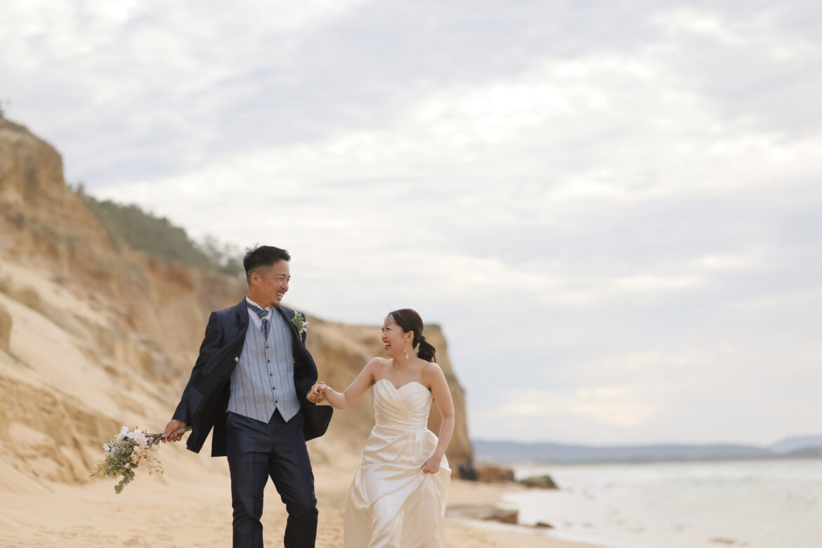 福岡の奈多海岸でウェディングドレスとタキシード姿の新郎新婦が手をつなぐ前撮り写真