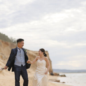 福岡の奈多海岸でウェディングドレスとタキシード姿の新郎新婦が手をつなぐ前撮り写真